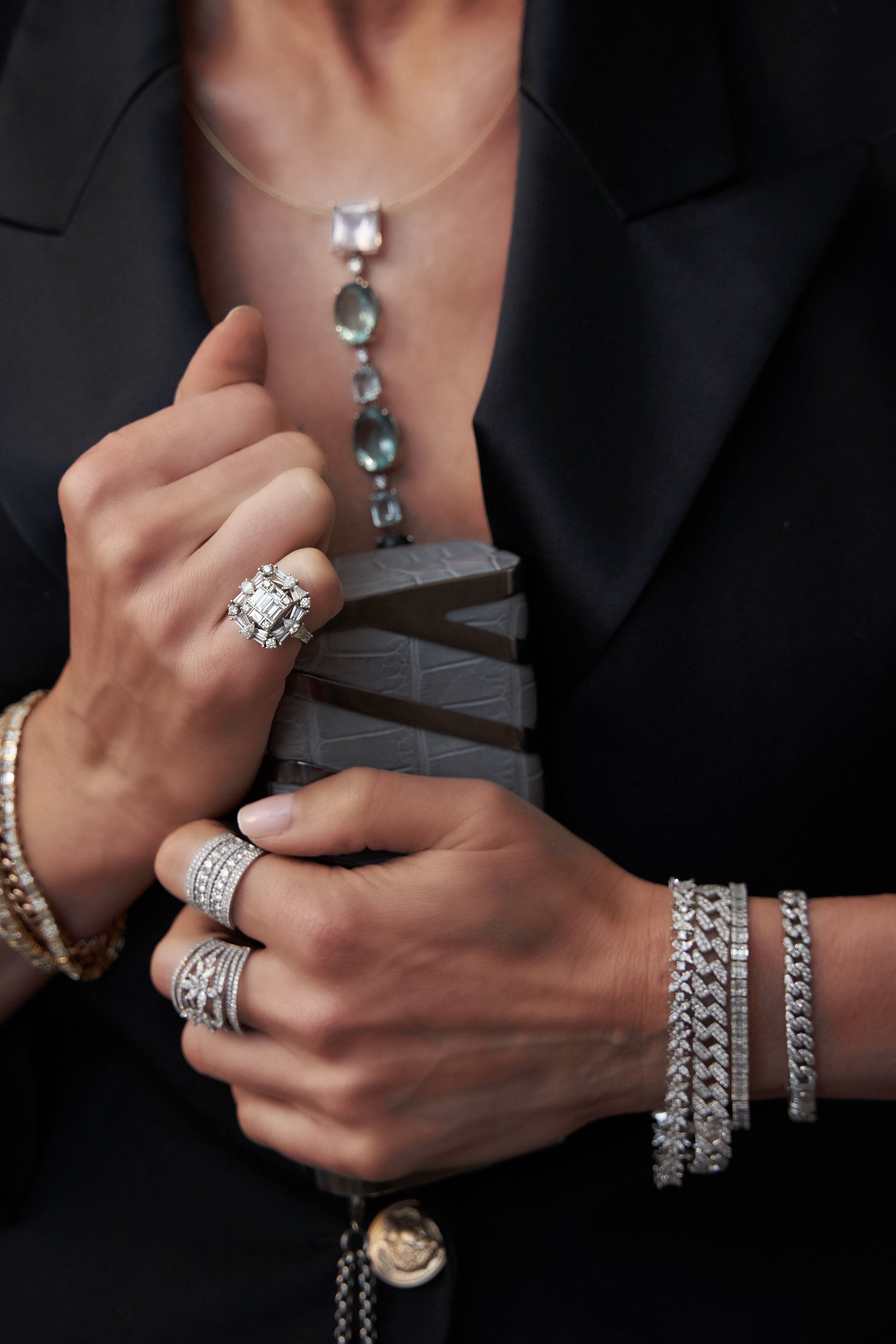Photoshoot style image of woman wearing rings, bracelets and holding a handbag. 